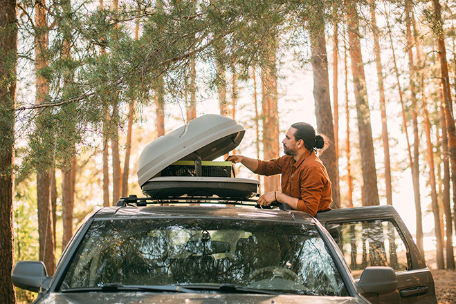Mężczyzna wyjmuje akcesoria campingowe z bagażnika dachowego samochodu zaparkowanego w lesie